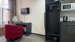 Une chambre compacte dotée d’une kitchenette, d’un téléviseur à écran plat fixé au mur, d’une chaise rouge et d’un ventilateur.