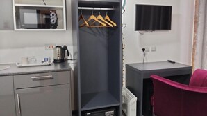 Une chambre d’hôtel compacte comprenant un coin cuisine, une armoire, un bureau et une chaise rose.