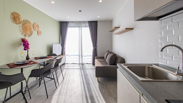 Cozinha moderna com pia de aço inoxidável, área de refeições com mesa e cadeiras, e sala de estar com sofá.