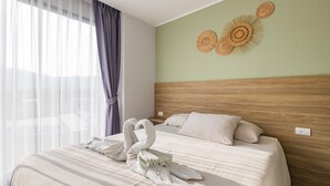 Quarto de hotel com cabeceira de madeira, cama com roupa de cama branca e um objeto decorativo sobre a cama.
