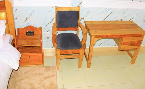 Une chambre à coucher comprenant un lit, un bureau en bois, une chaise, une table de chevet et une petite table d’appoint.