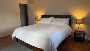 A neatly made bed with white linens in a room with wooden flooring. There are two bedside tables with lamps.