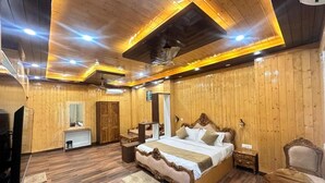 A spacious bedroom with a large bed, wooden walls, a ceiling fan, and a small desk area. - The Chail Pine Orchard Resort (Chail)