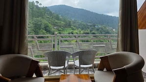 A balcony with wicker chairs and a table, overlooking a lush green valley and hills. - The Chail Pine Orchard Resort (Chail)