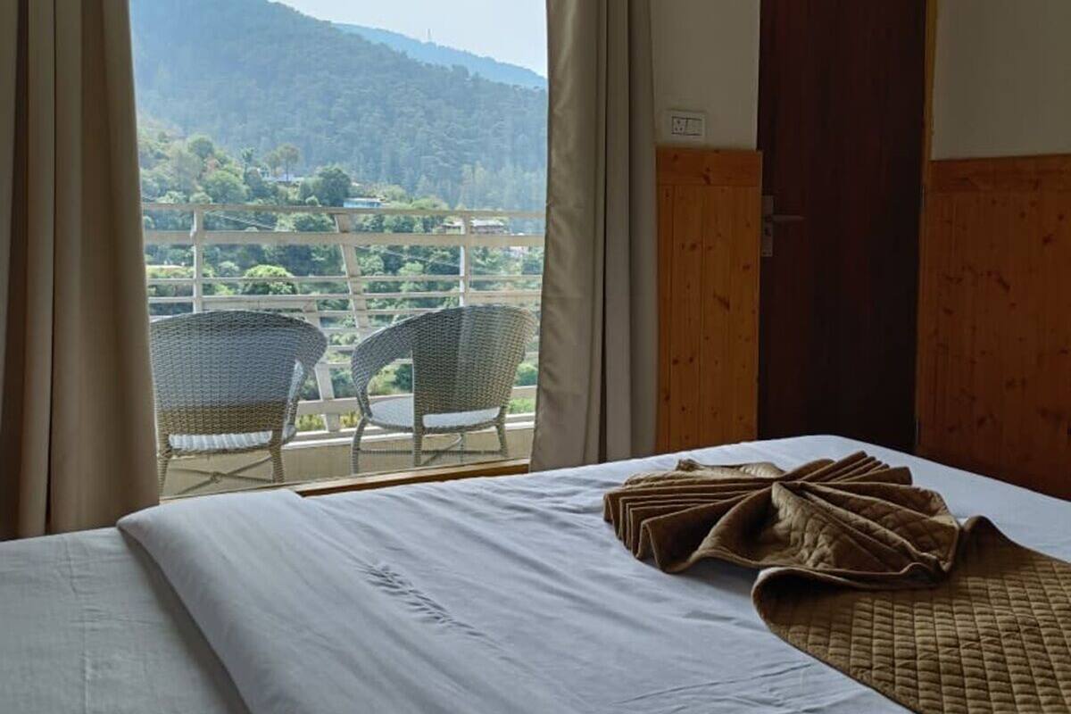 A hotel room with a bed, a window with curtains, a door, and a view of a landscape.