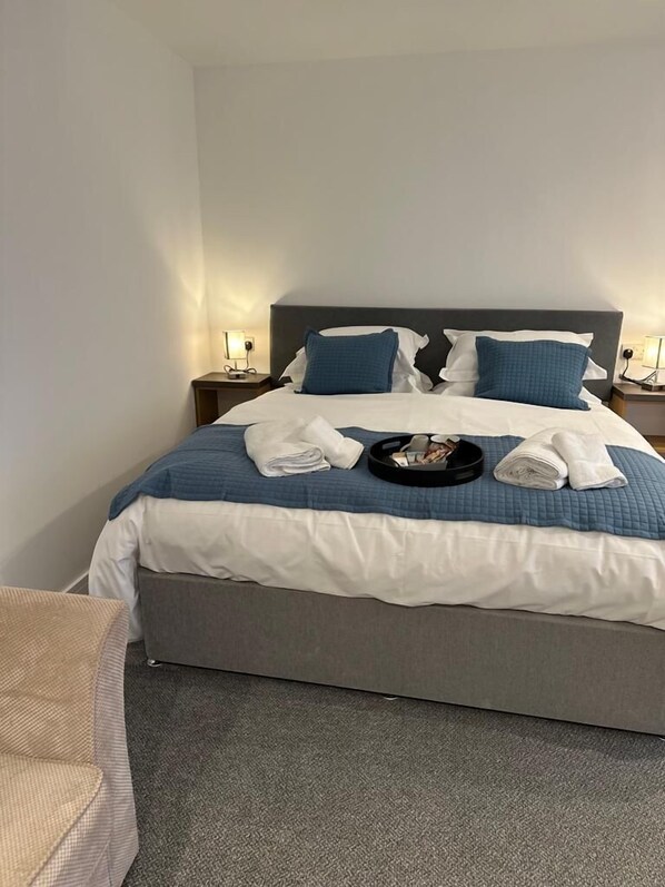 Un lit bien fait, avec une literie bleue et blanche, un plateau avec des serviettes et une tête de lit grise.