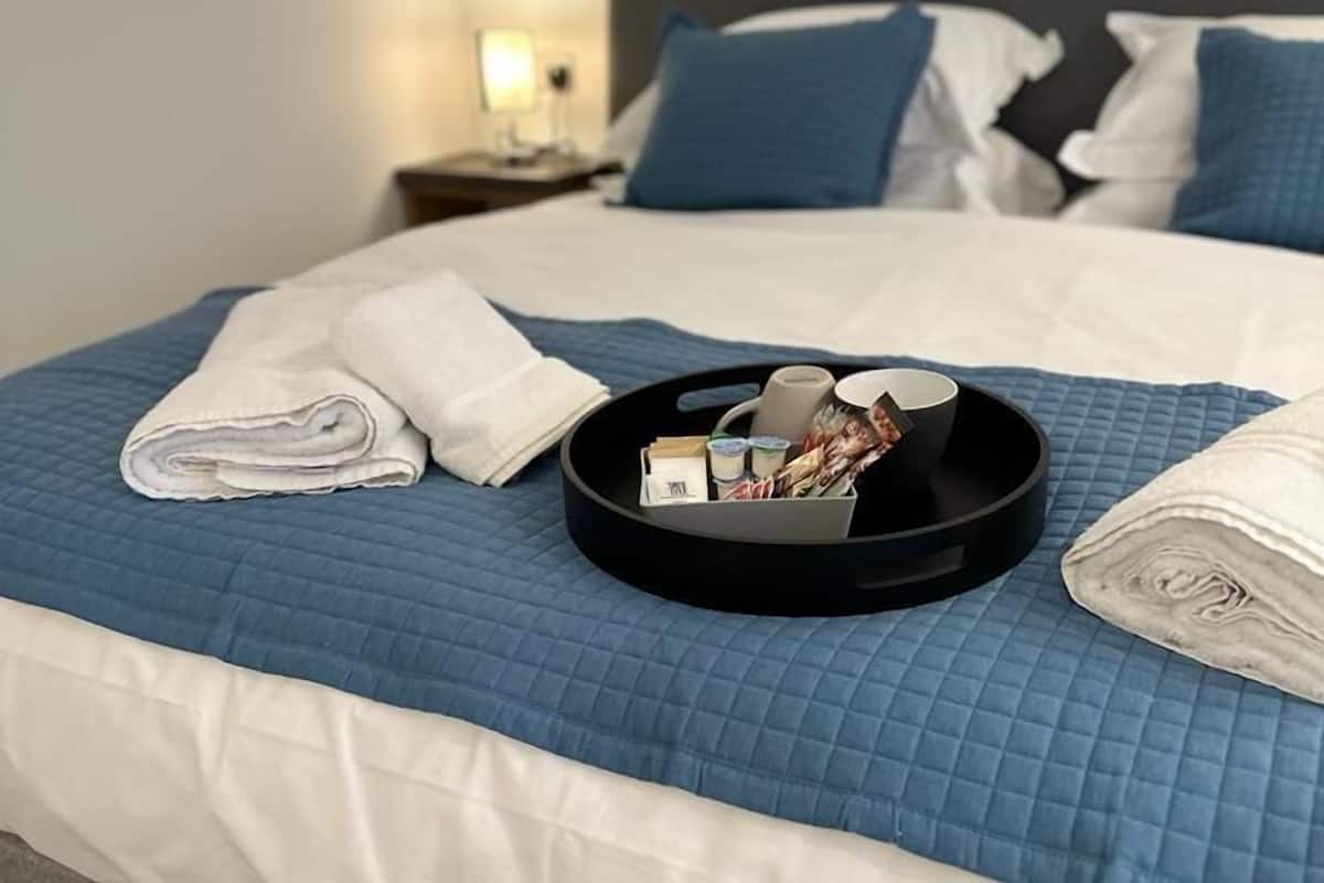A neatly made bed with a blue quilt, a tray with toiletries, and a folded towel.