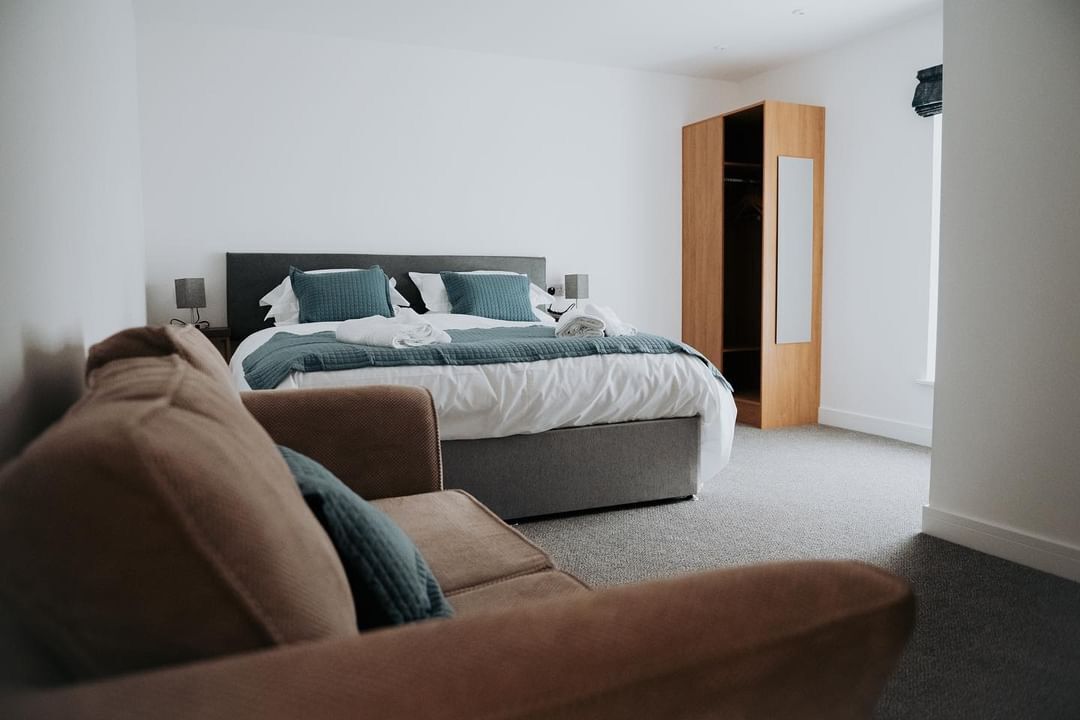 Un dormitorio moderno con cama, mesita de noche, armario de madera y sofá marrón.