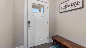 Une porte blanche avec une fenêtre, un banc et une pancarte « Bienvenue » accrochée au mur.