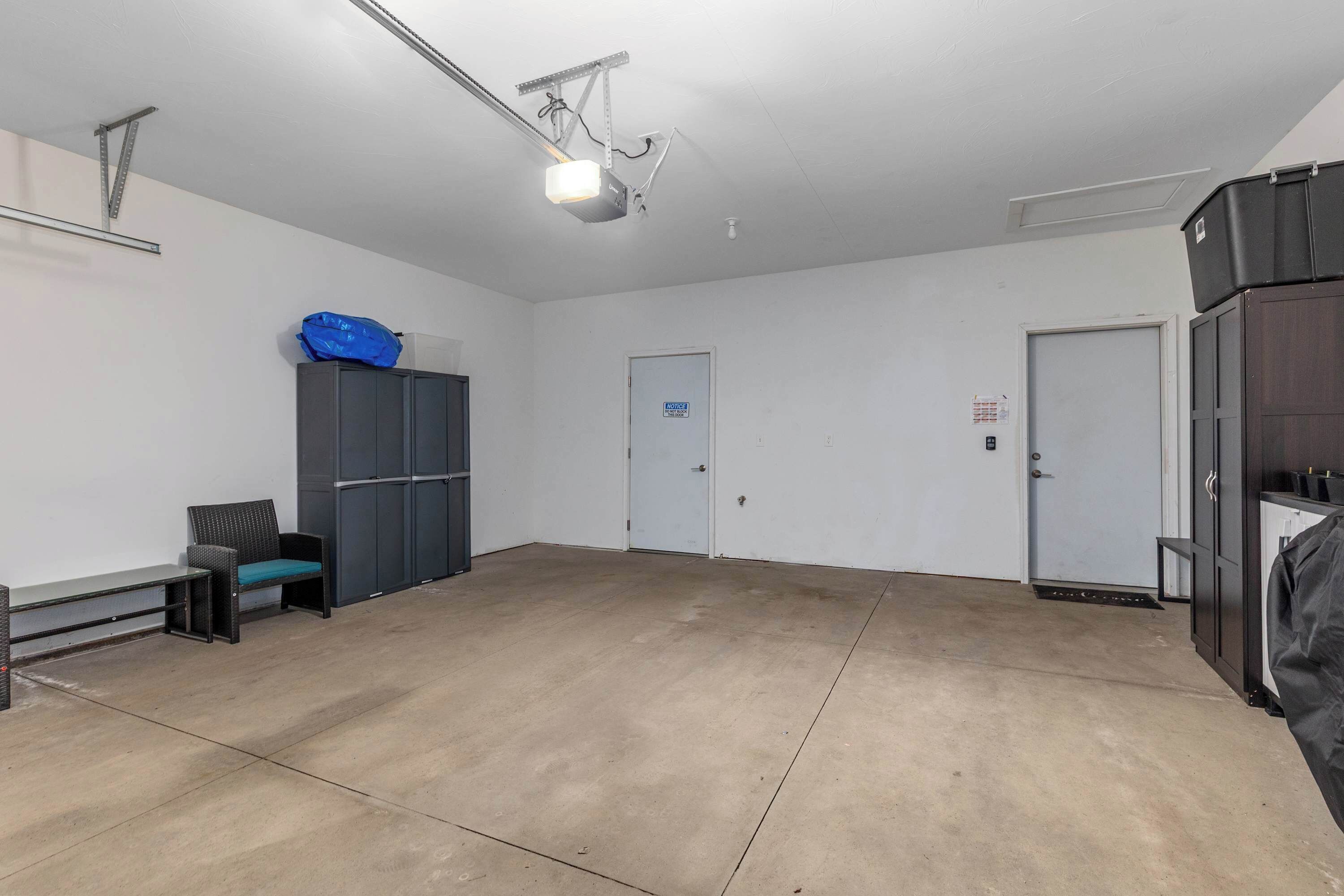 A spacious, well-lit room with a large concrete floor, a ceiling-mounted projector, a door with a blue sign, and a black cabinet.