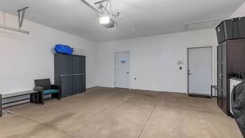 A spacious, well-lit room with a large concrete floor, a ceiling-mounted projector, a door with a blue sign, and a black cabinet.