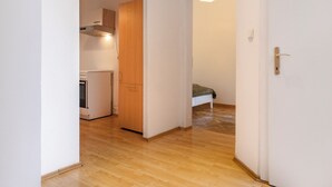 A narrow hallway with wooden flooring leading to a kitchen area with a refrigerator and wooden cabinets. - Bright 2BR Apt Perfect Long Stay (Vienna)