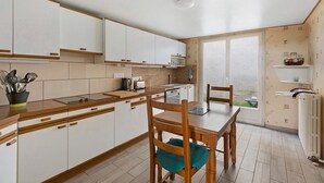 A kitchen with white cabinets, a wooden dining table, and a view through a glass door. - Gîte Du Centre with Private Terrace and Wi-Fi (Romorantin-Lanthenay)