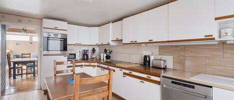 A modern kitchen with white cabinets, a wooden dining table, and a built-in dishwasher.