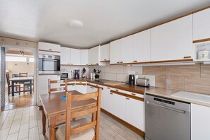 Une cuisine moderne avec des meubles blancs, une table à manger en bois et un lave-vaisselle encastré.
