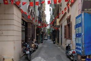 A narrow street with parked motorcycles and scooters, buildings with traditional architecture, and red flags hanging overhead.
