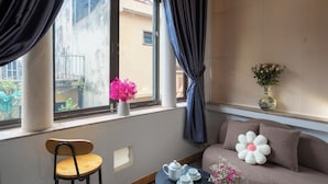 A cozy room with a sofa, a small table, a chair, a window with curtains, and a vase with flowers. - Homestay PW Hoang Sam (Hanoi)