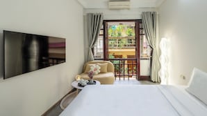 A hotel room with a bed, a TV mounted on the wall, a small table with a vase of flowers, and a view of a balcony with plants. - Homestay PW Hoang Sam (Hanoi)