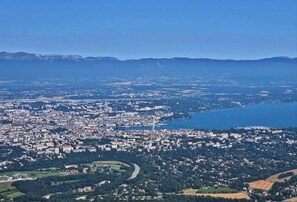 Una vista aerea di una città costiera con un mix di zone urbane e rurali, che include un fiume, campi e un'ampia distesa d'acqua.