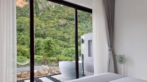 A modern bedroom with a large bed, a white bathtub, and a view of a lush green landscape. - Red Cheek Mountain Villa  (Krabi)