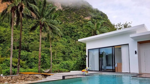 A modern pool area with a floating tray of drinks, surrounded by lush greenery and a mountain backdrop. - Red Cheek Mountain Villa  (Krabi)