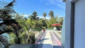 A view from a balcony overlooking a pool area with palm trees and a clear sky. - Feel at home in paradise/ A few minutes from the beach. (Nuevo Vallarta)