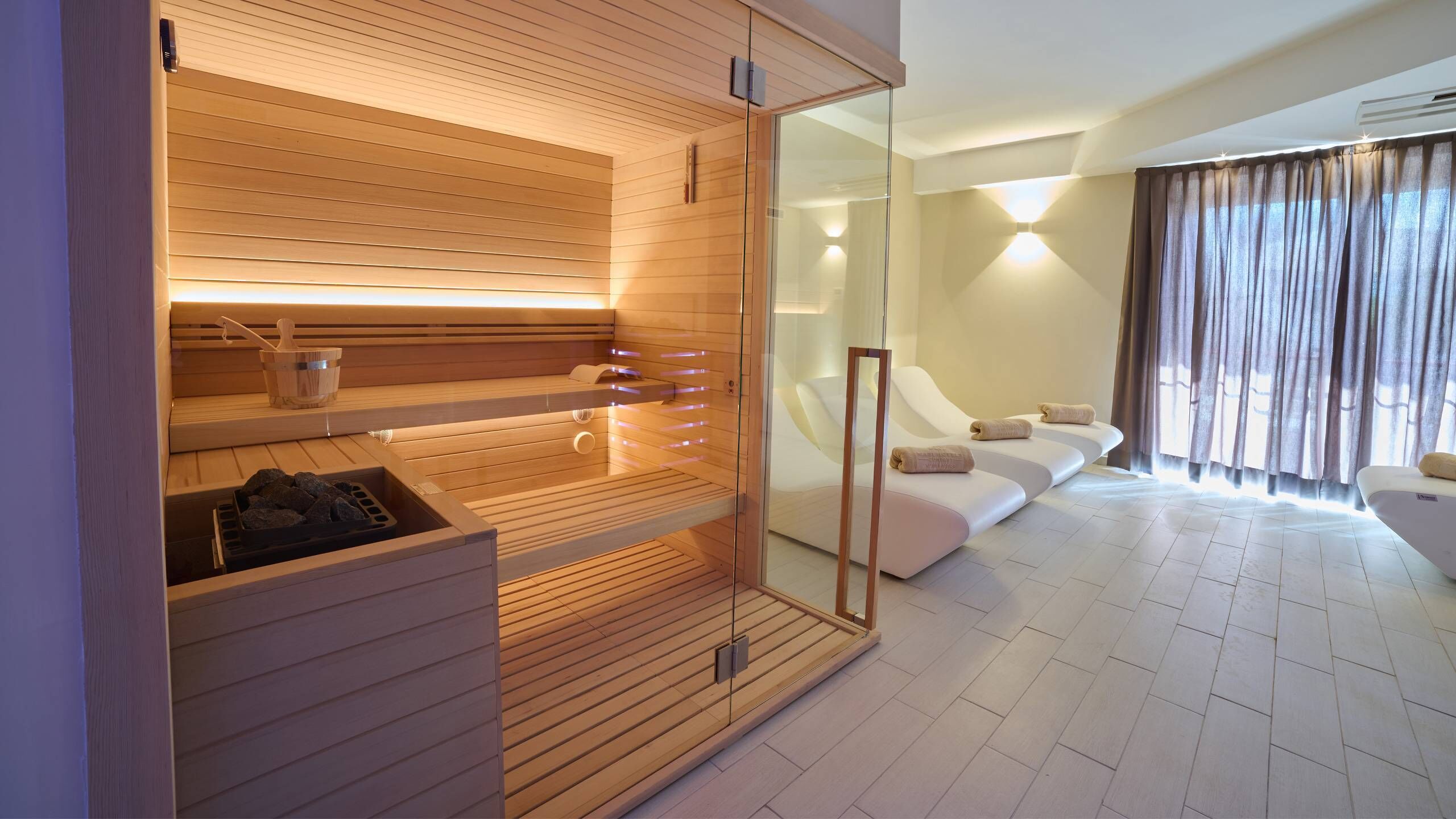Een moderne spa-ruimte met houten lambrisering, een glazen wand en een witte bank met handdoeken.