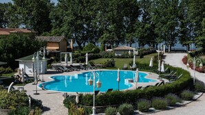 Una piscina rodeada de sillas de descanso y sombrillas, con vistas a un lago y árboles al fondo.