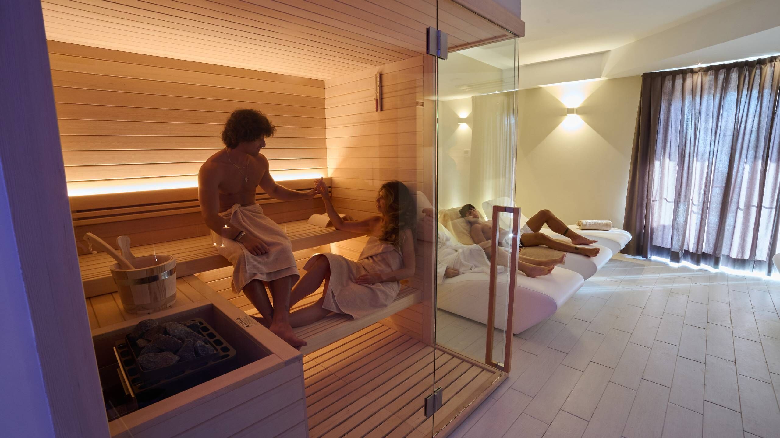 A modern spa room with wooden paneling, a glass partition, and a relaxation area with a sofa.