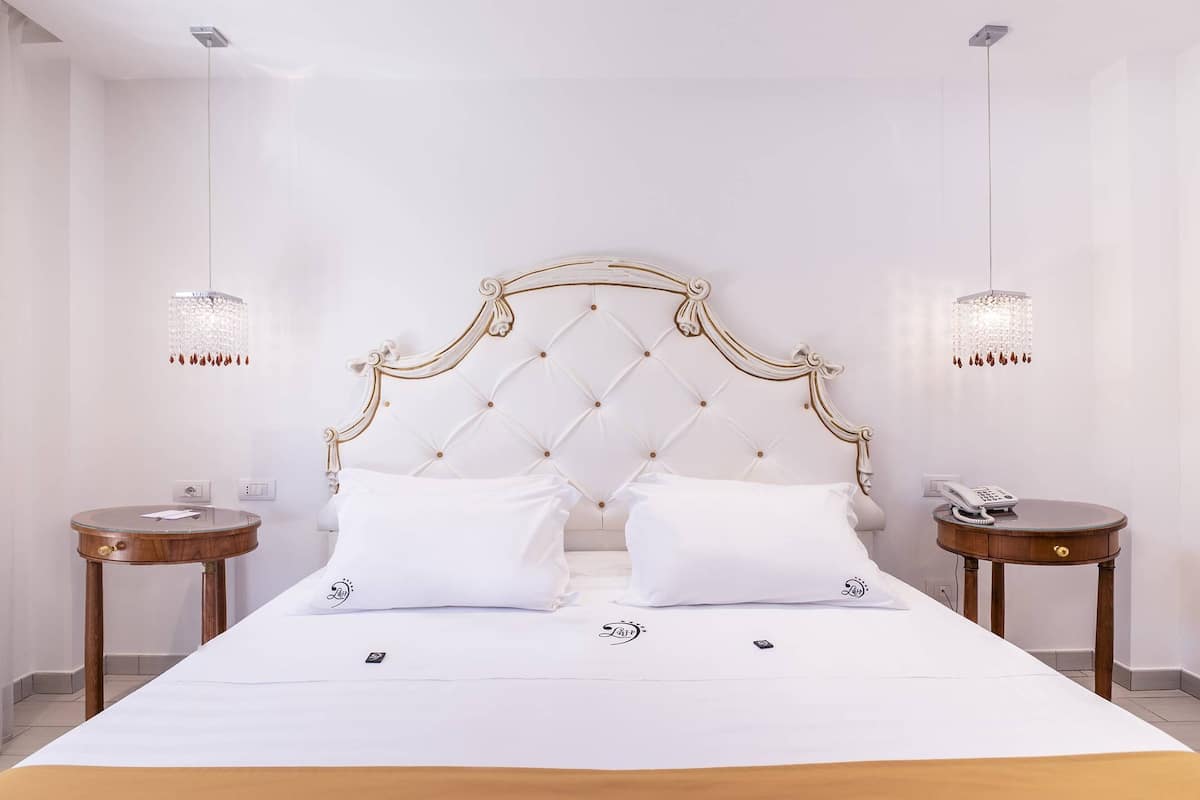 Una habitación de hotel con una cama grande, dos mesitas de noche y dos lámparas fijadas a la pared.