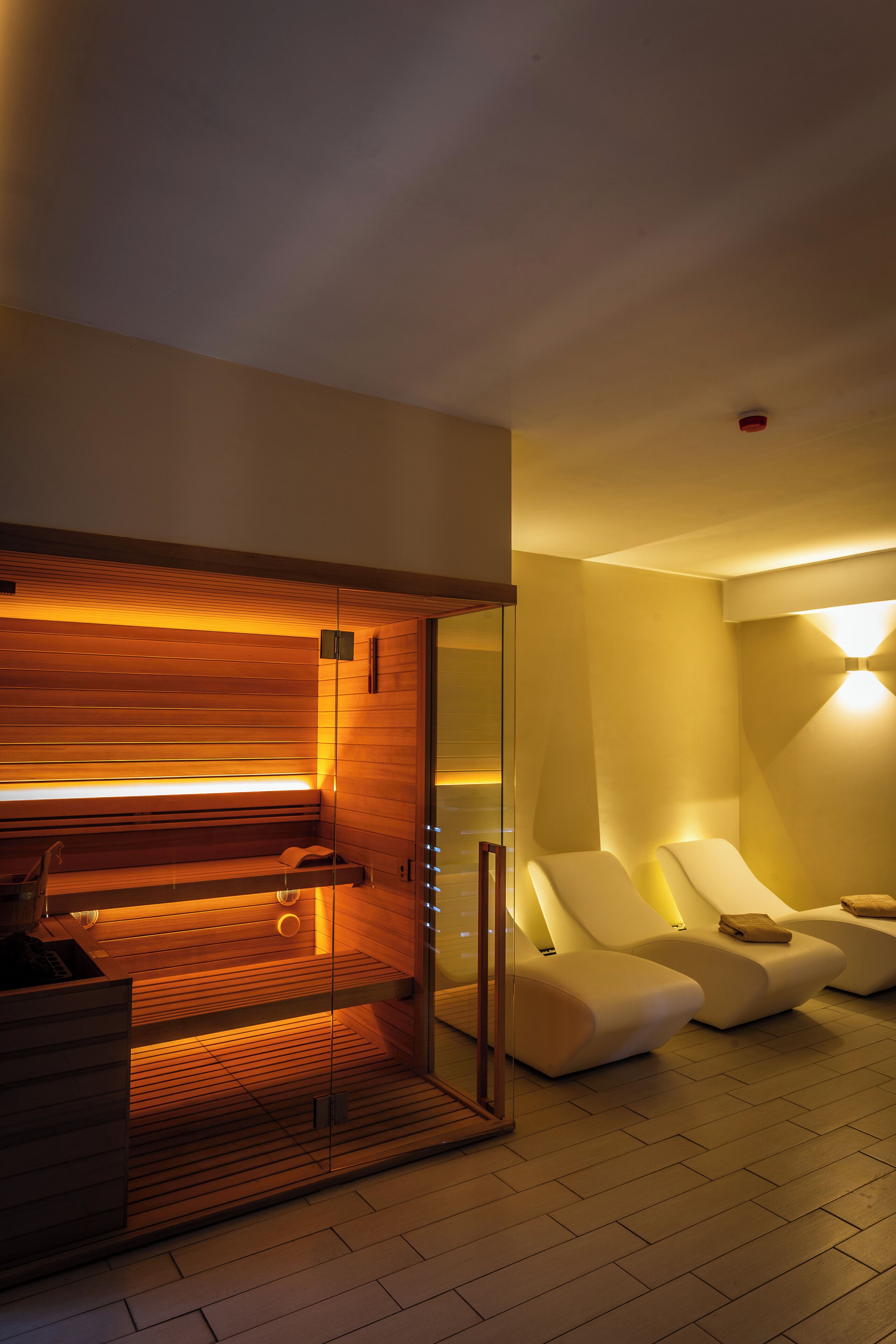 A modern spa room with a wooden sauna, glass-enclosed relaxation area, and ambient lighting.