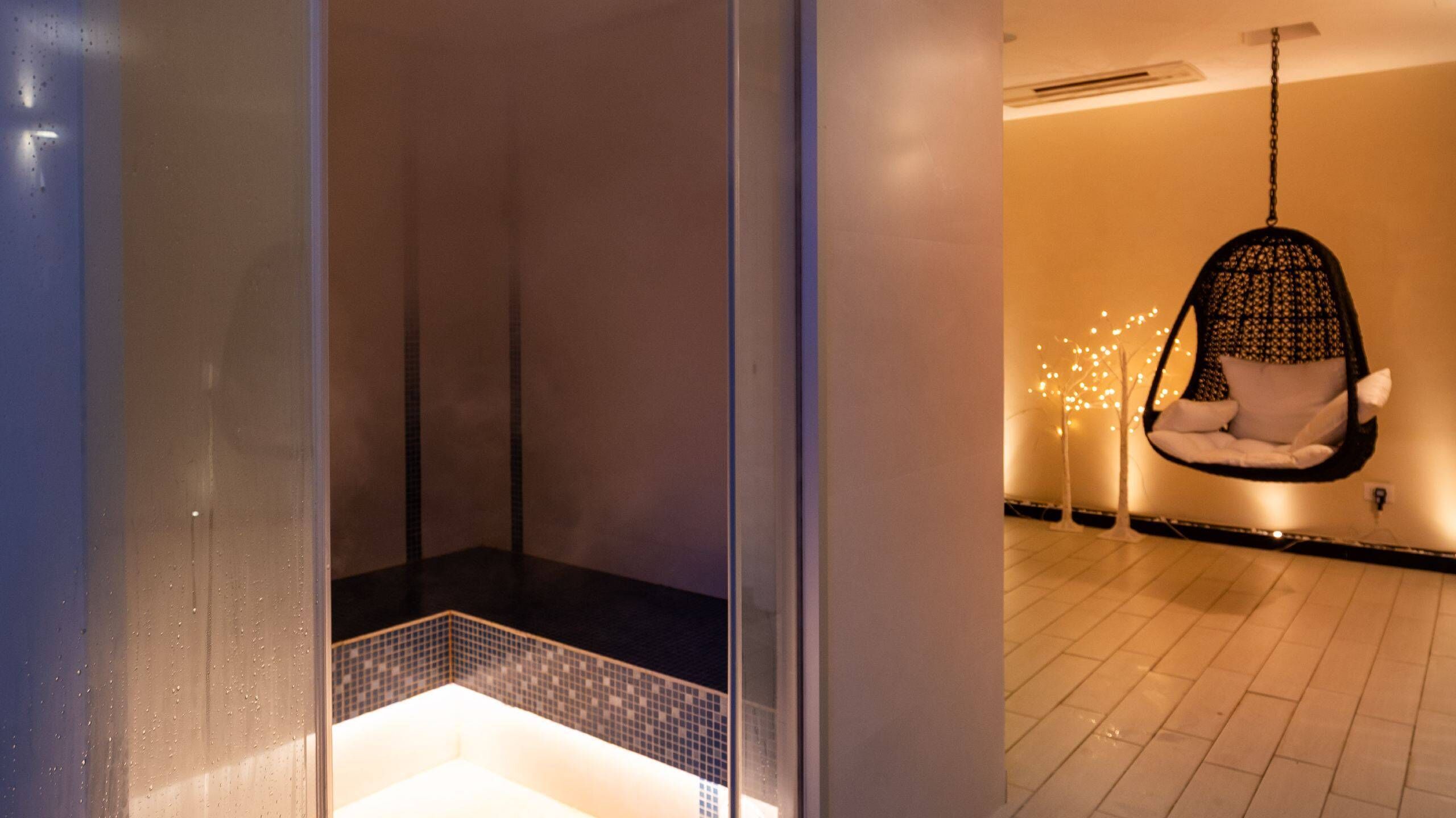 A modern bathroom with a glass shower enclosure, a hanging chair with a cushion, and a tiled floor.