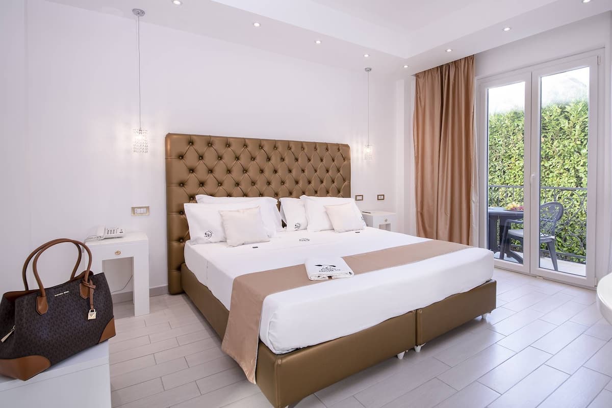 Una habitación de hotel con una cama grande, un escritorio, una silla, un bolso de mano y un balcón con vistas.