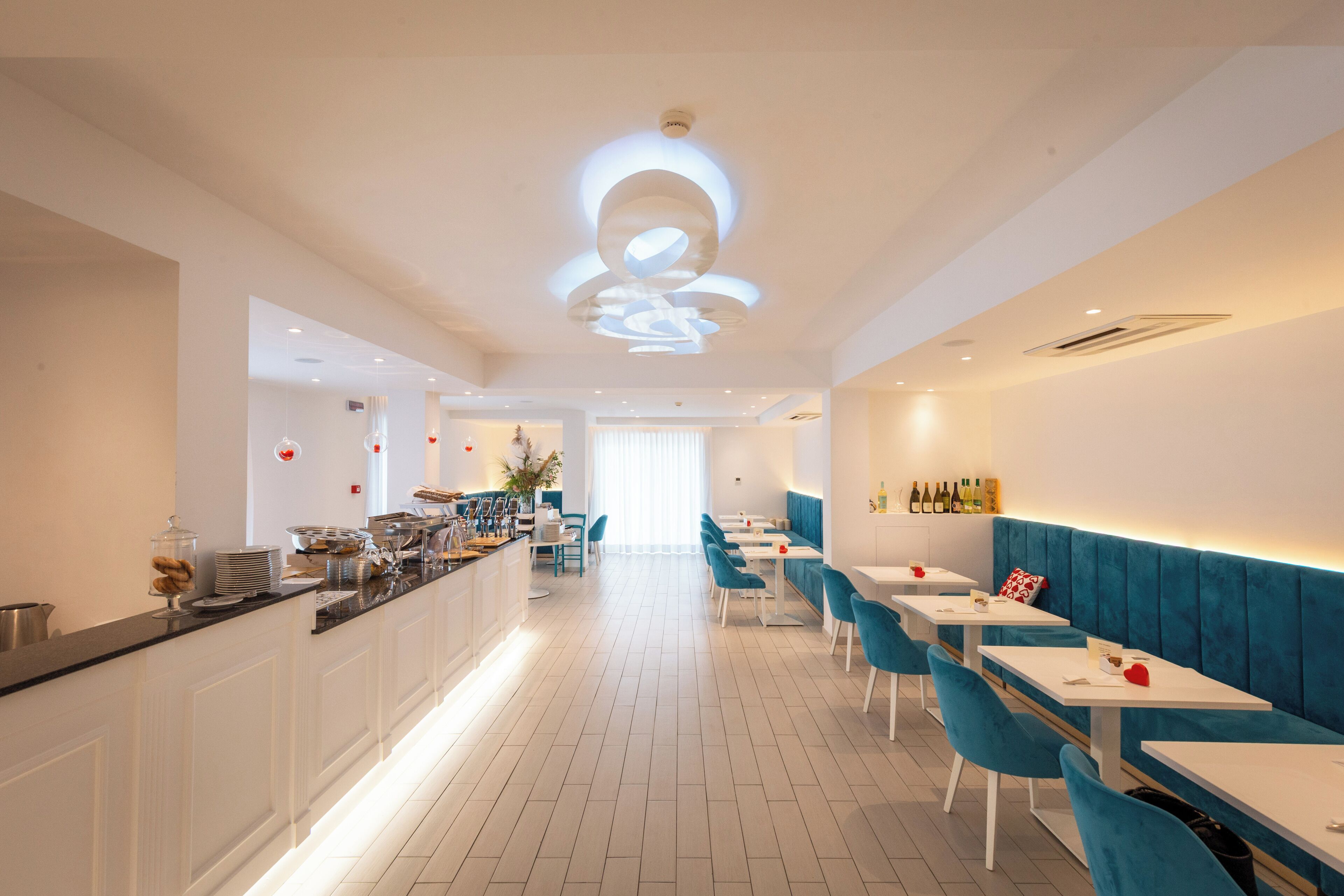 A modern restaurant with a long counter, blue chairs, and white tables.