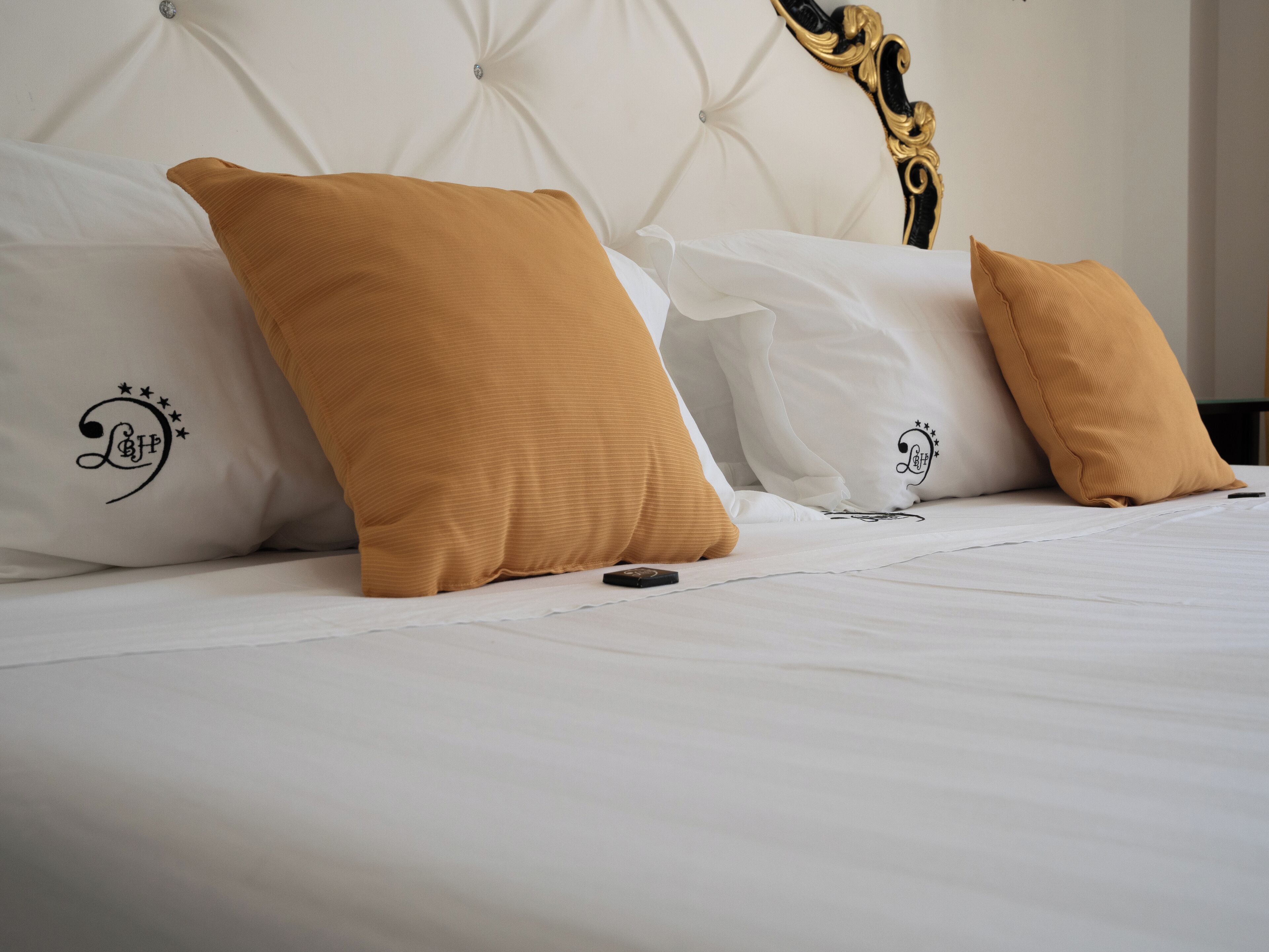 A bed with white bedding and three mustard-colored pillows with embroidered designs.