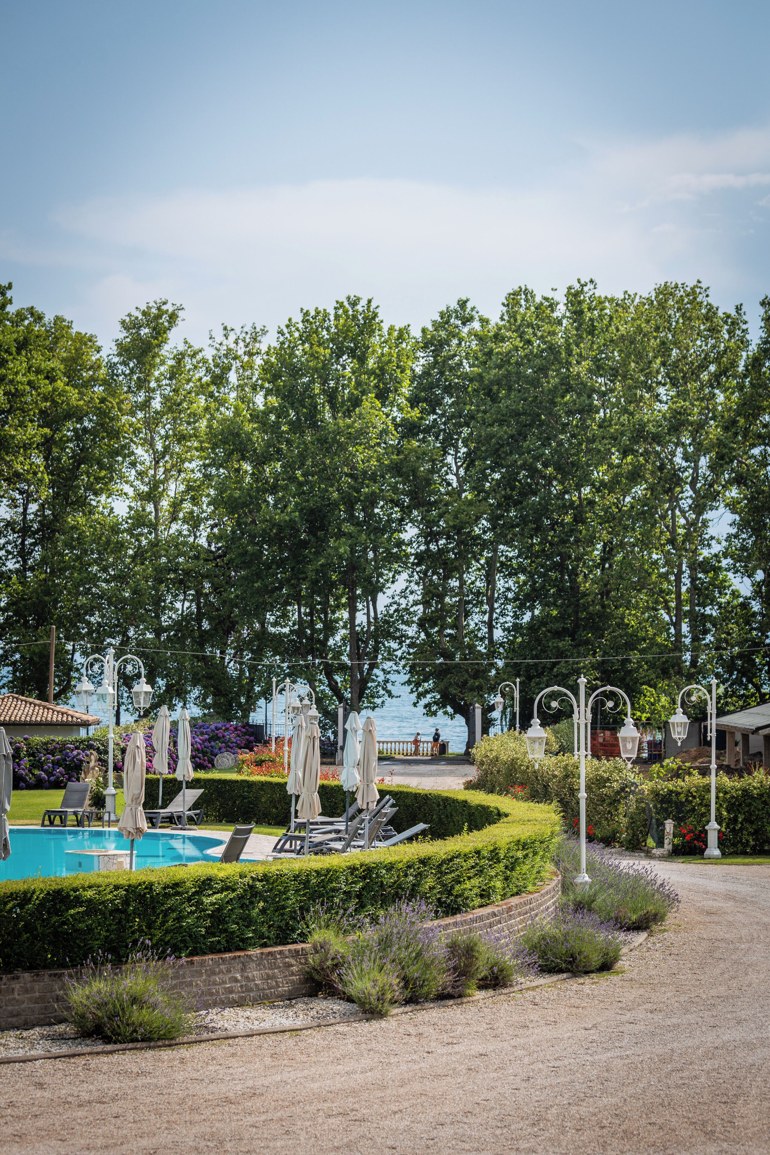 A pool area with lounge chairs and umbrellas, surrounded by well-maintained hedges and trees.