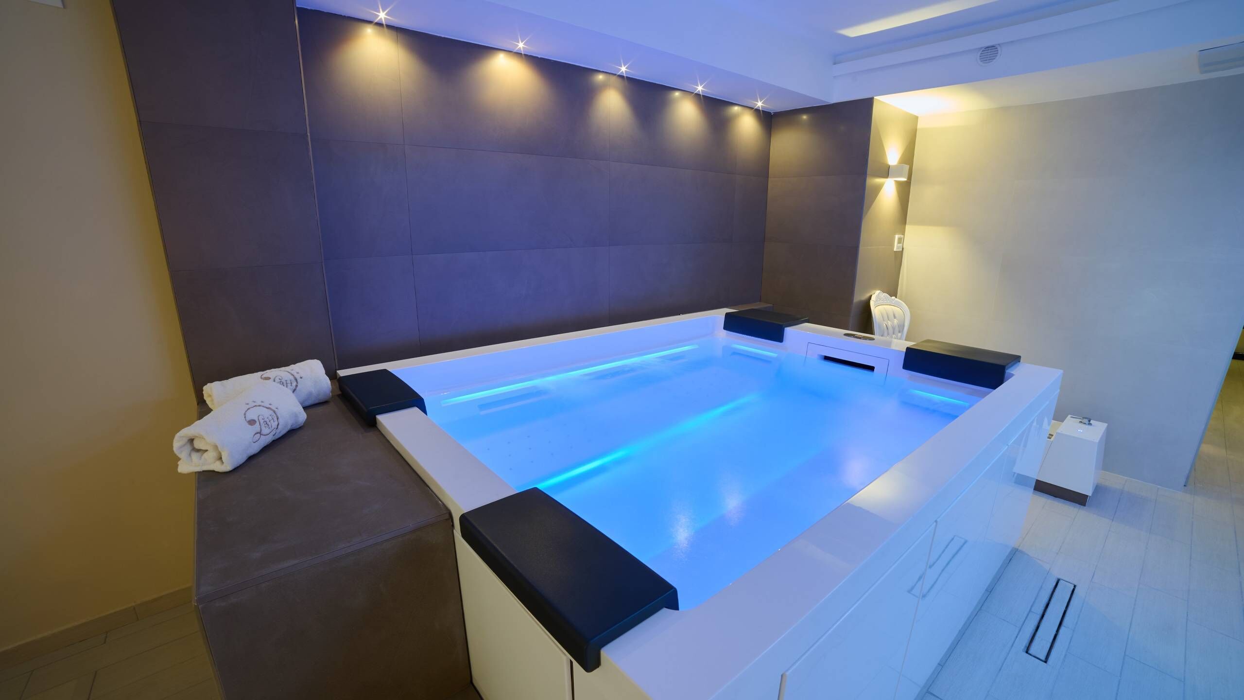 Um spa moderno com uma banheira grande e retangular, uma toalha e uma cadeira de massagem fixada na parede.