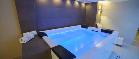 Um spa moderno com uma banheira grande e retangular, uma toalha e uma cadeira de massagem fixada na parede.
