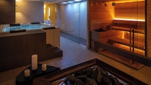 Un moderno espacio de spa con mostrador de recepción, una bañera de piedra climatizada y una pared de madera con camilla de masaje.
