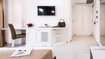 Une chambre d’hôtel moderne avec un bureau blanc, un téléviseur à écran plat, un fauteuil en cuir marron et un lit recouvert d’une couverture blanche.