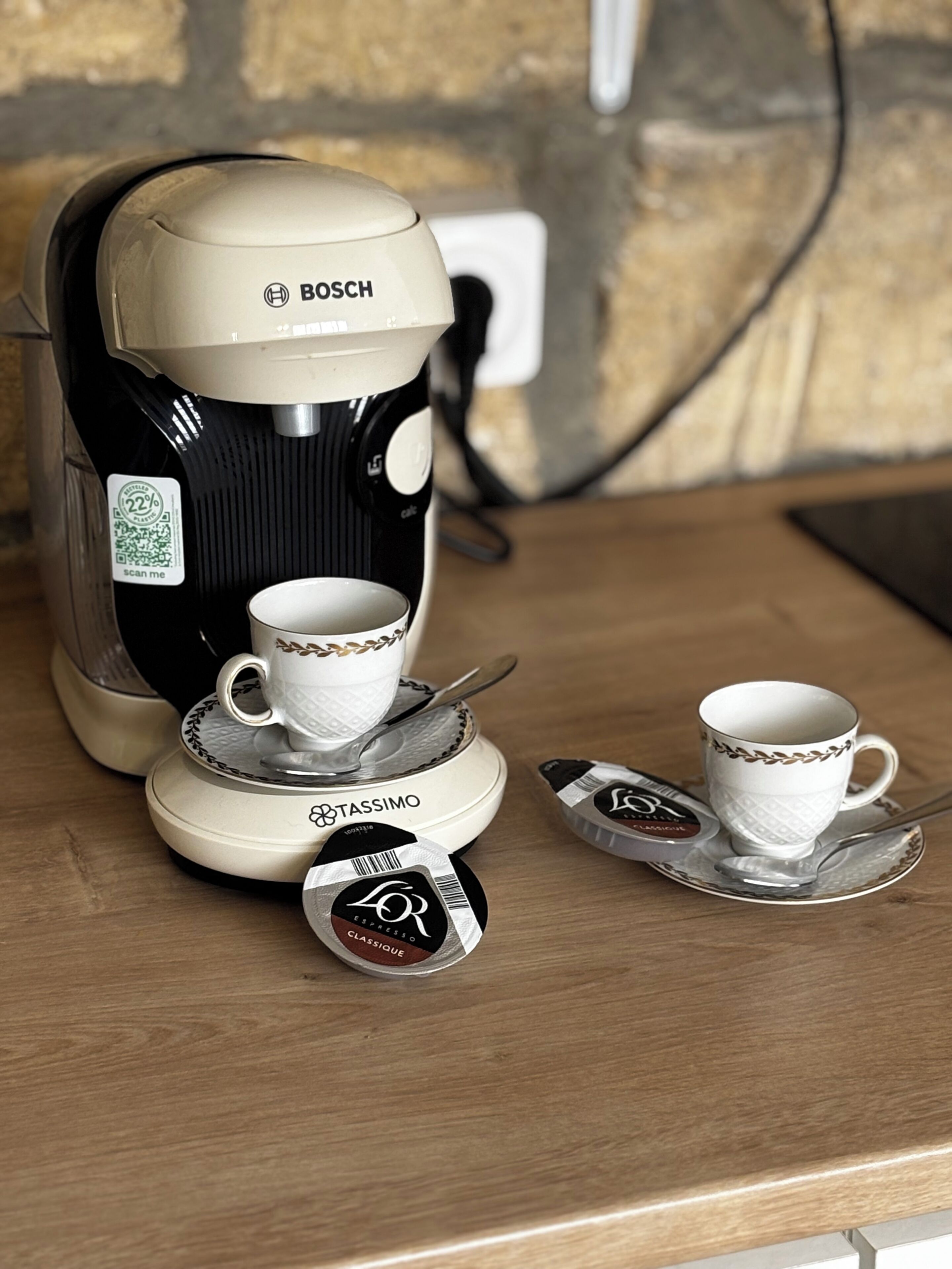 Una cafetera con dos tazas y una cuchara sobre una mesa de madera.