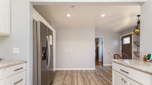 Une cuisine moderne avec des meubles blancs, un réfrigérateur en acier inoxydable et un plancher en bois.