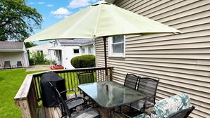 Une terrasse en bois avec une table et des chaises en verre, un parasol et un barbecue.