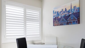 Une pièce moderne avec une table en verre, deux chaises noires, un canapé blanc et un tableau représentant un paysage urbain accroché au mur.