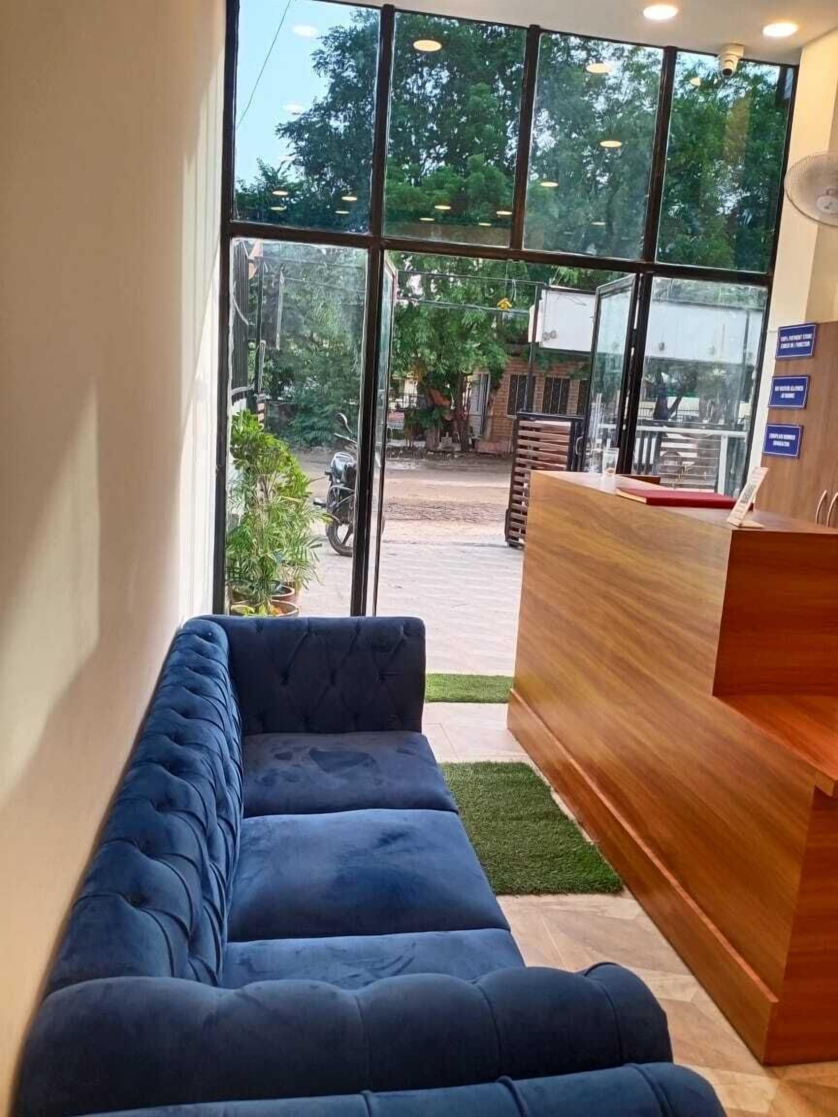 A reception area with a blue sofa, a wooden reception desk, and large windows offering a view of the street and greenery outside.