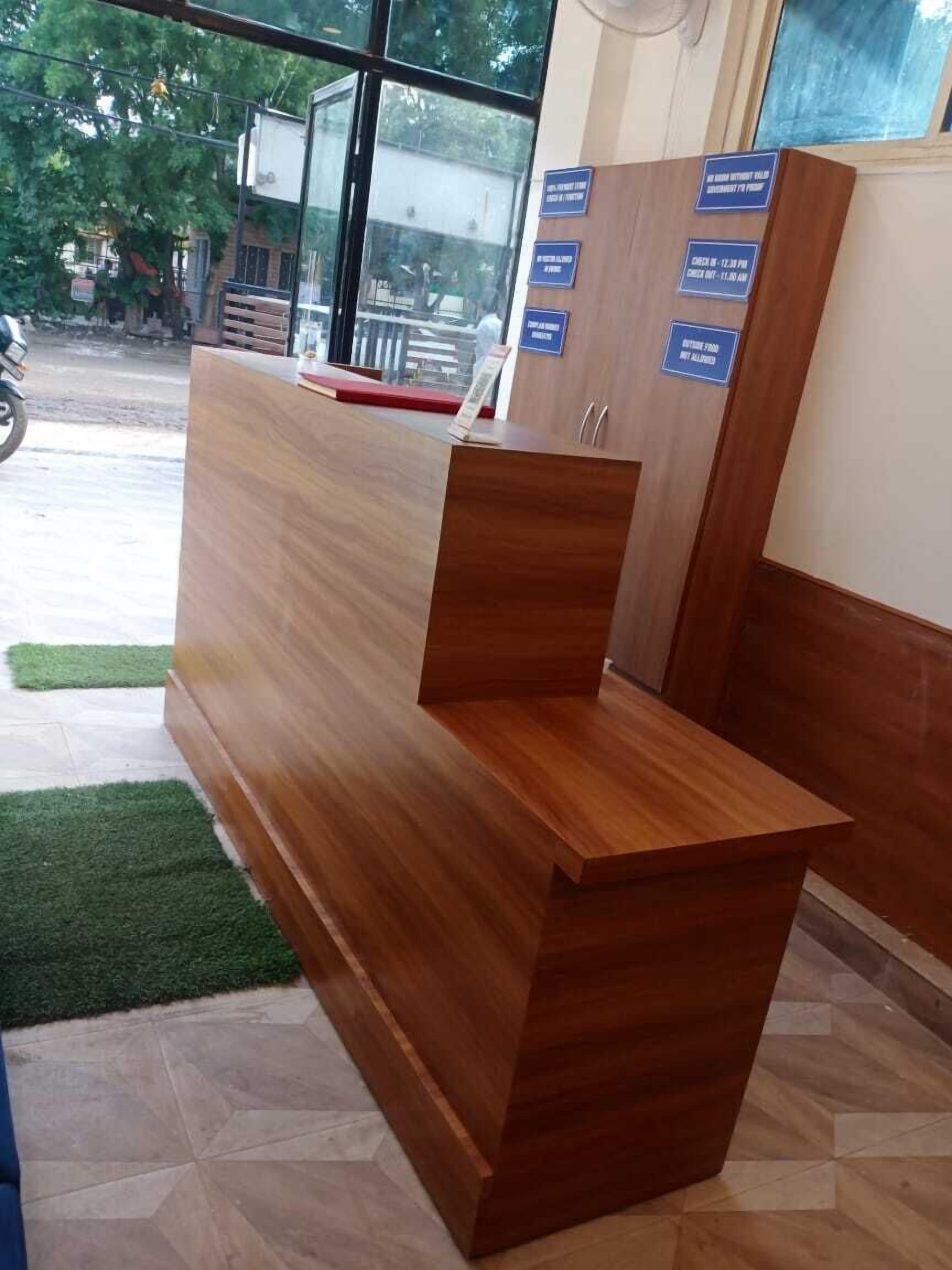 A reception desk with a wooden finish, a glass window, and a sign indicating check-in times.