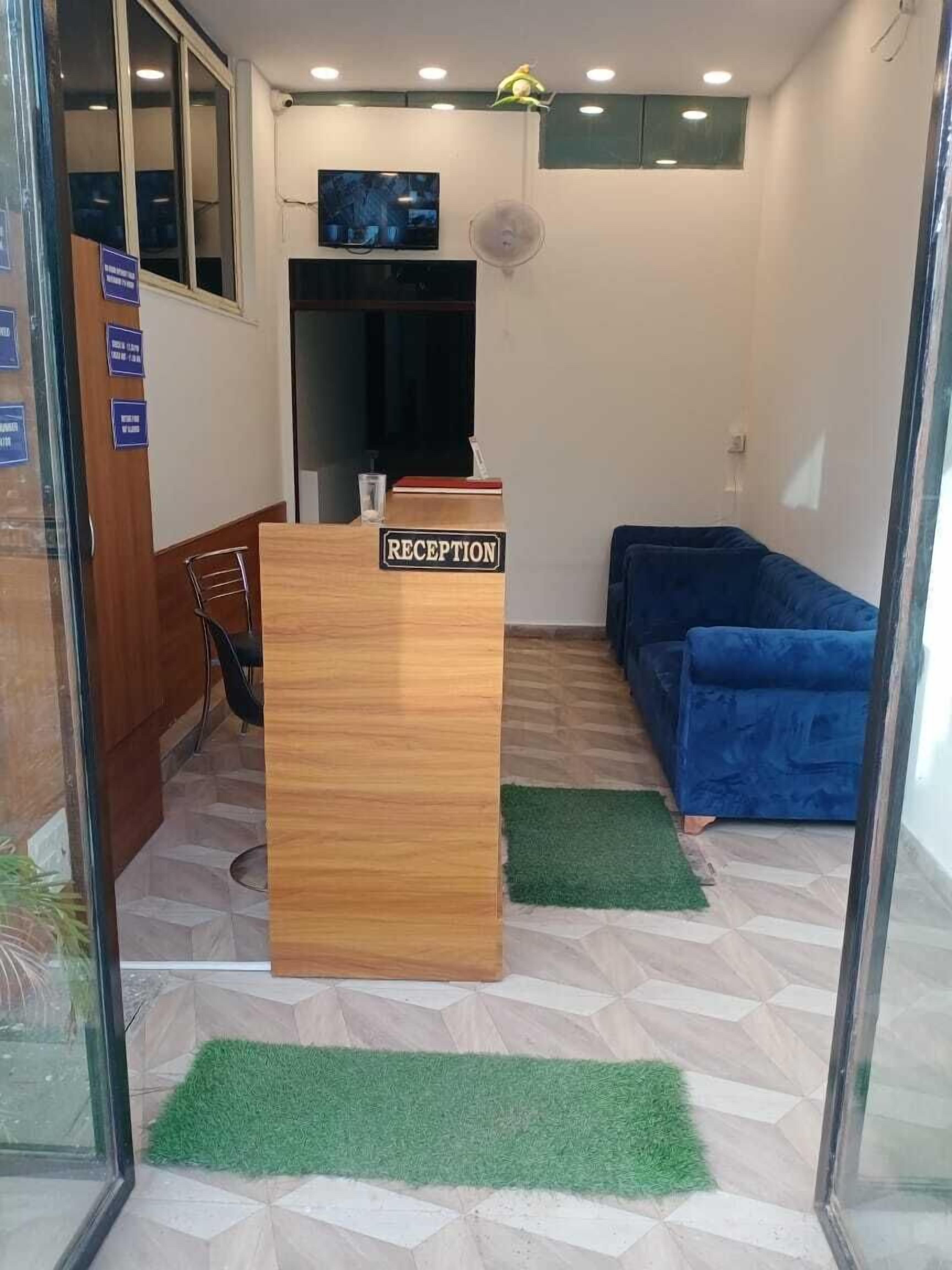 Ett receptionsområde med ett skrivbord i trä där det står "RECEPTION", en blå soffa och en tv som är monterad på väggen.