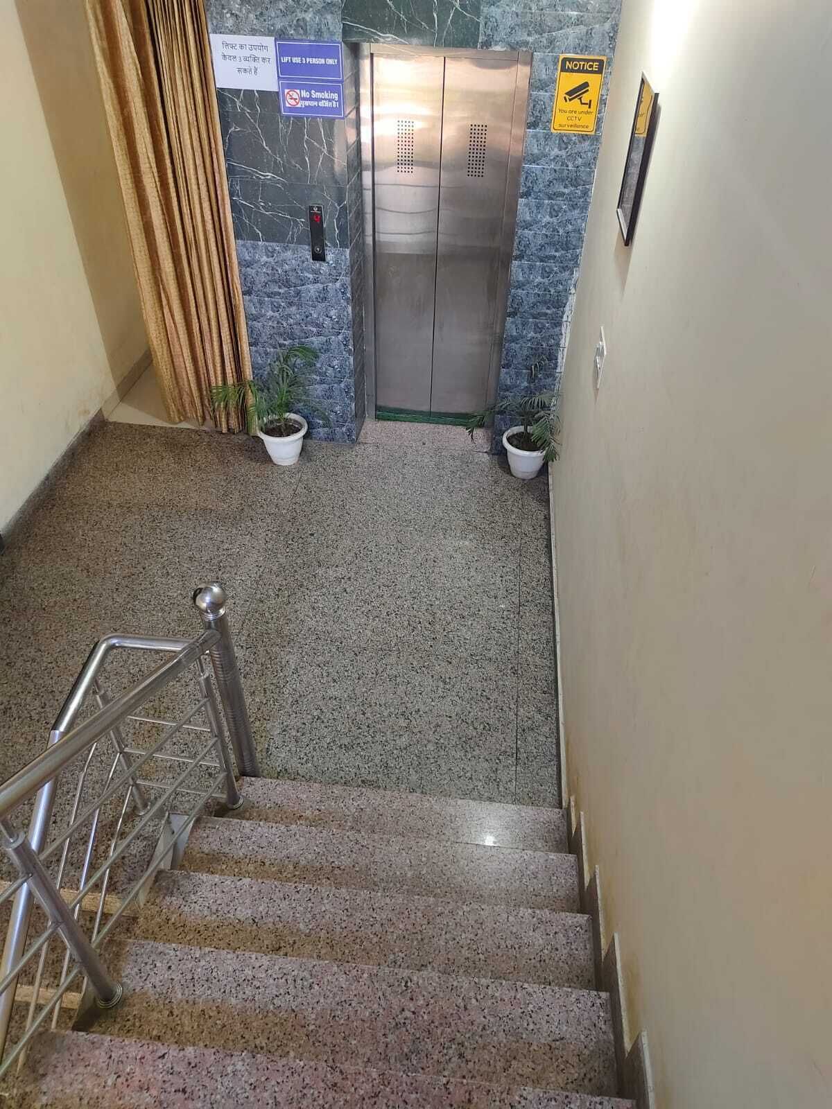 A staircase leading to an elevator with a marble wall and a notice sign.