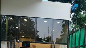A reception area with a wooden desk, glass doors, and potted plants. - The Experia  Boutique hotel  (Jaipur)