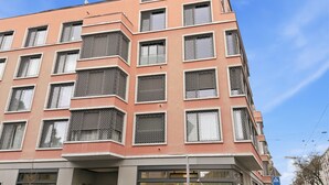 A multi-story building with a ground-floor shop, balconies, and a clear sky. - Comfortable 1BR flat / great location - Baron 44 (Zürich)